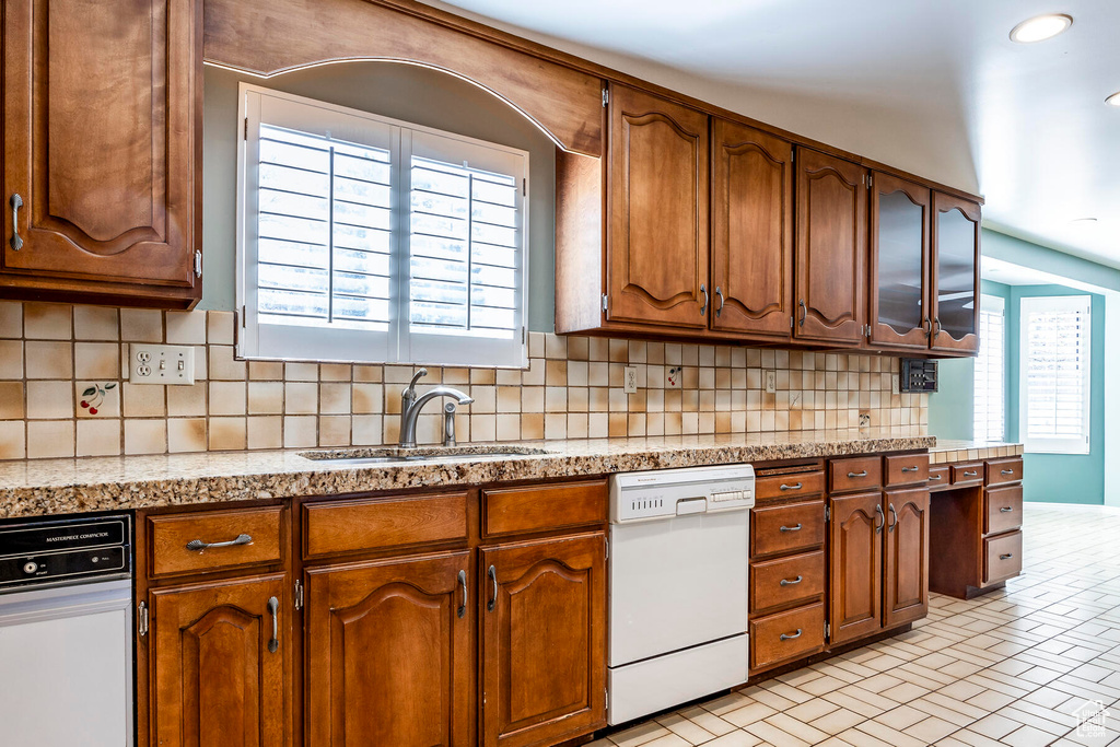 Kitchen with light tile flooring, sink, backsplash, and white dishwasher