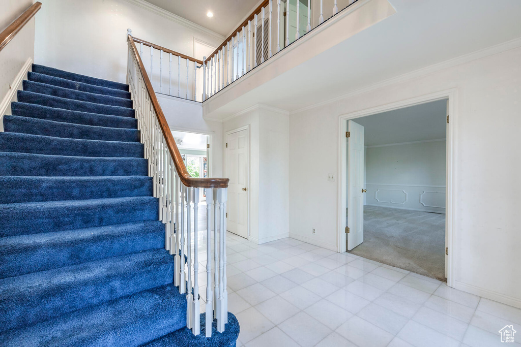 Stairway featuring crown molding, light tile floors, and a high ceiling