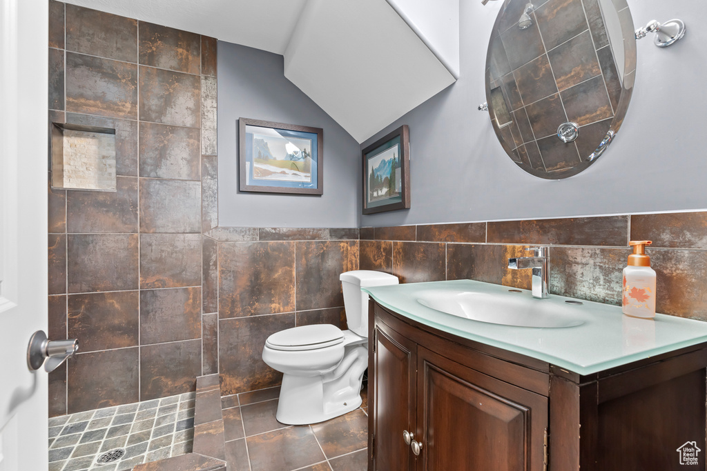 Bathroom with tile walls, a shower, toilet, vanity, and tile floors