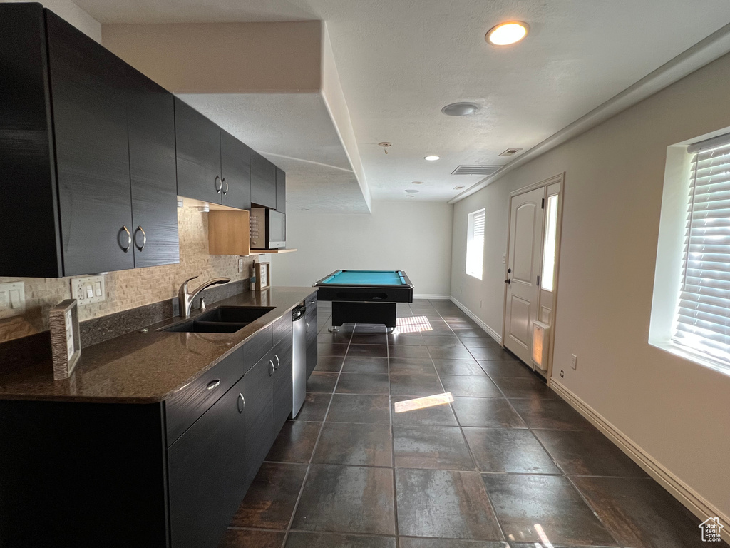 Kitchen with dark tile floors, stainless steel appliances, pool table, sink, and tasteful backsplash