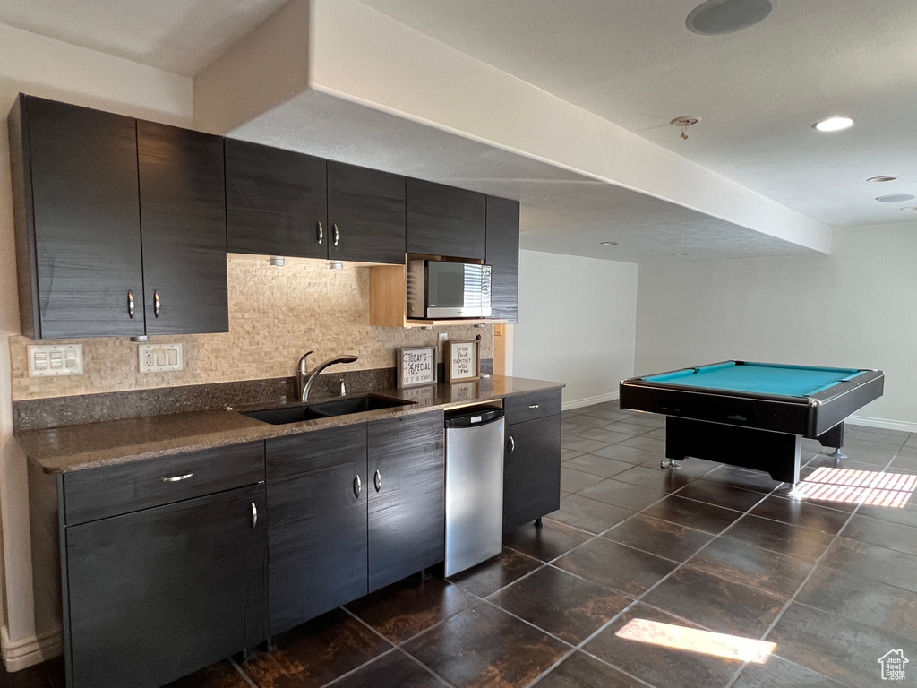 Kitchen with stainless steel dishwasher, billiards, tasteful backsplash, sink, and dark tile floors