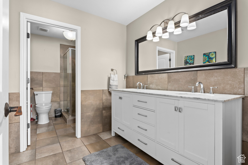 Bathroom with tile walls, a shower with door, tile floors, and double sink vanity