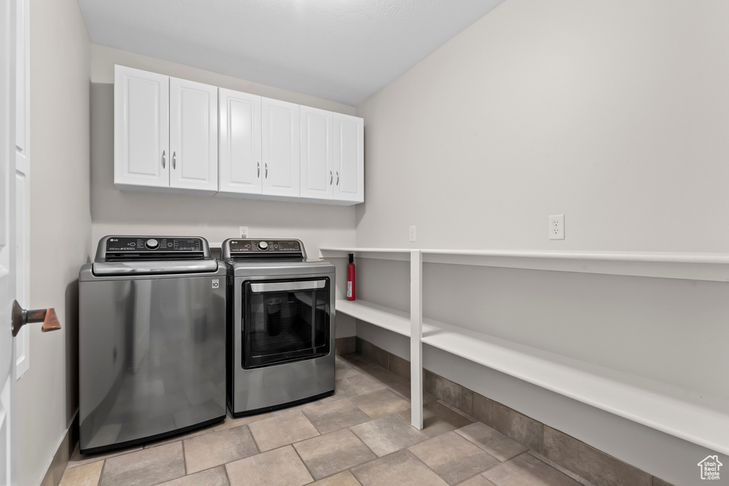 Laundry room featuring cabinets, washing machine and dryer, and light tile flooring