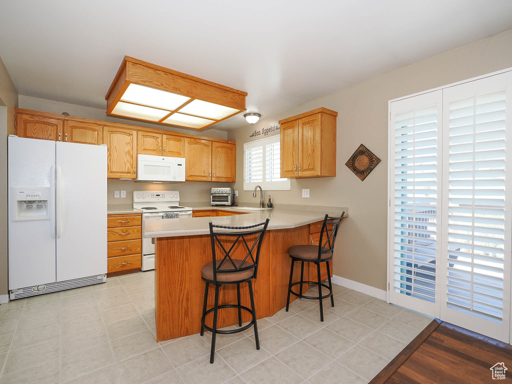 Kitchen featuring kitchen peninsula, white appliances, a breakfast bar, sink, and light tile floors