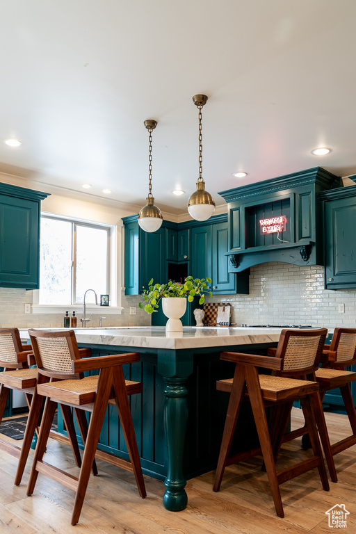 Kitchen featuring a breakfast bar, sink, light hardwood / wood-style floors, backsplash, and pendant lighting