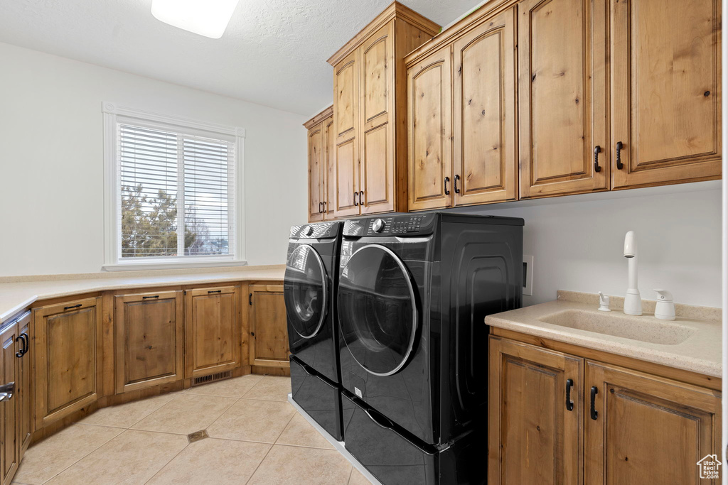 Clothes washing area featuring cabinets, sink, washing machine and dryer, and light tile floors