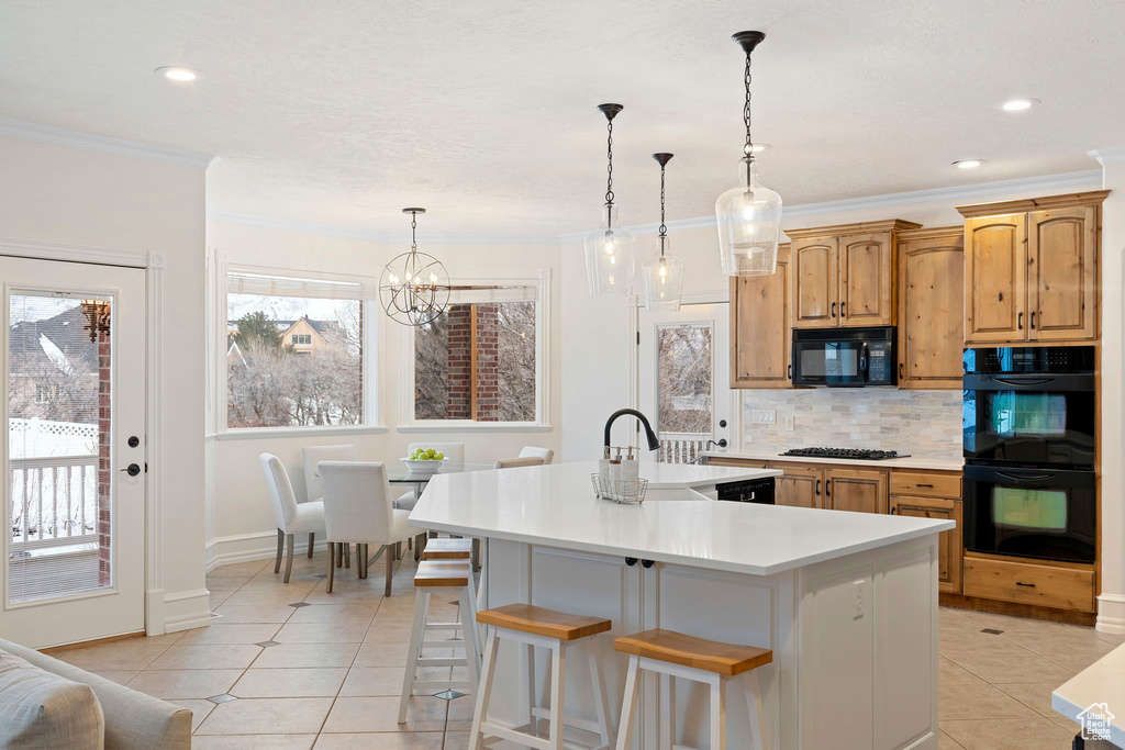 Kitchen with light tile floors, tasteful backsplash, a breakfast bar area, decorative light fixtures, and black appliances
