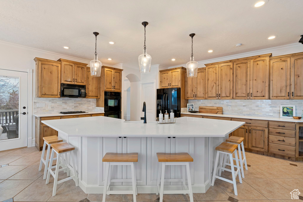 Kitchen featuring a kitchen island with sink, black appliances, a kitchen bar, and decorative light fixtures