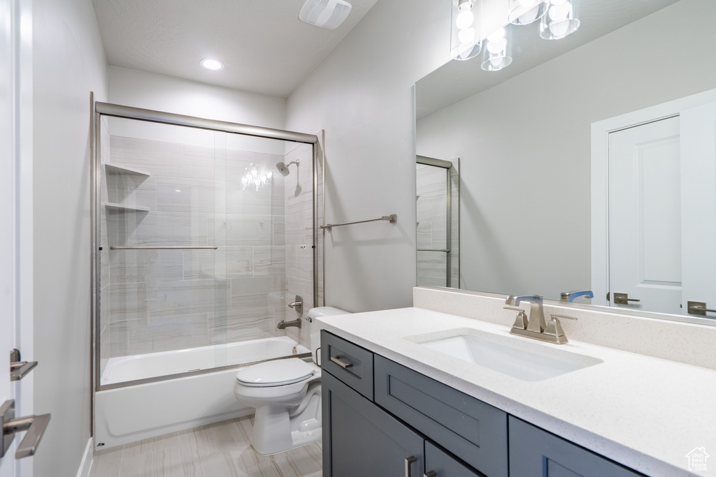 Full bathroom featuring tile flooring, vanity, toilet, and bath / shower combo with glass door