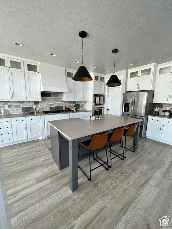 Kitchen with light hardwood / wood-style floors, stainless steel appliances, white cabinetry, and a center island with sink