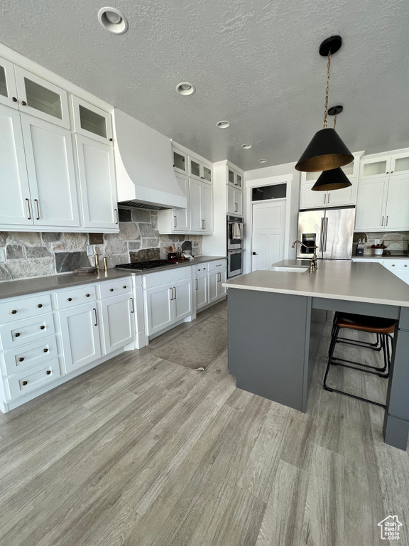 Kitchen with white cabinets, a center island with sink, appliances with stainless steel finishes, and pendant lighting