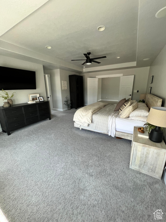 Bedroom with ceiling fan, a raised ceiling, and dark colored carpet