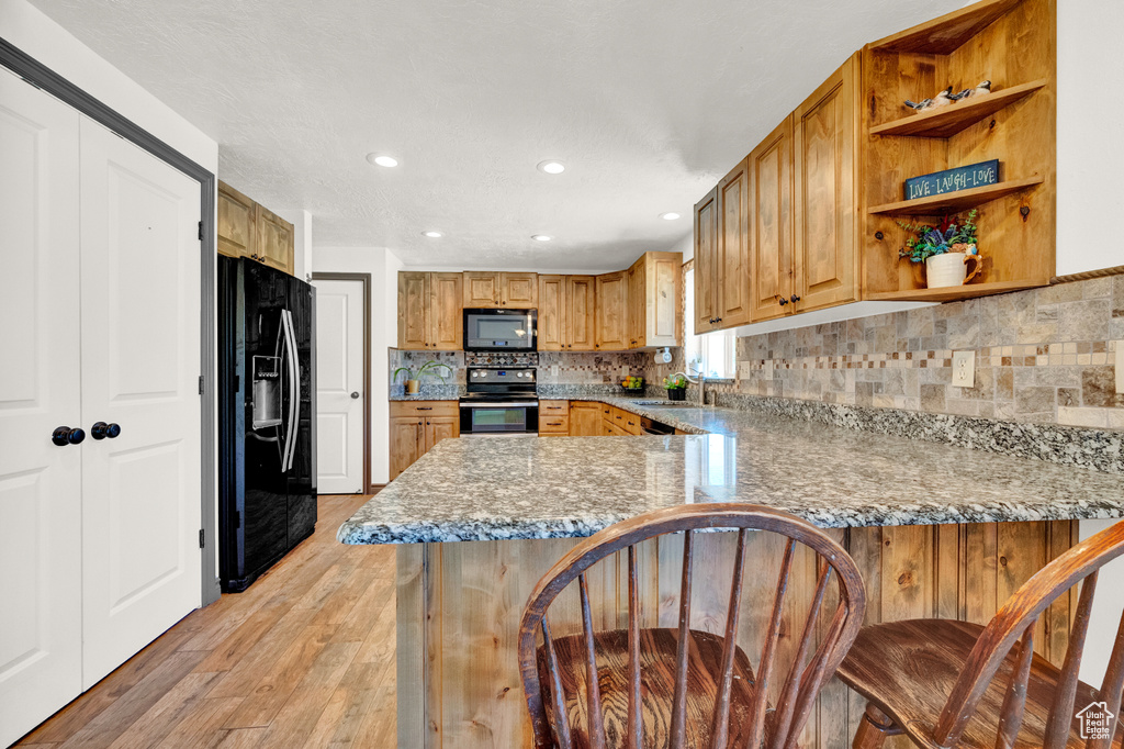 Kitchen with kitchen peninsula, light hardwood / wood-style floors, range with electric stovetop, black refrigerator with ice dispenser, and tasteful backsplash