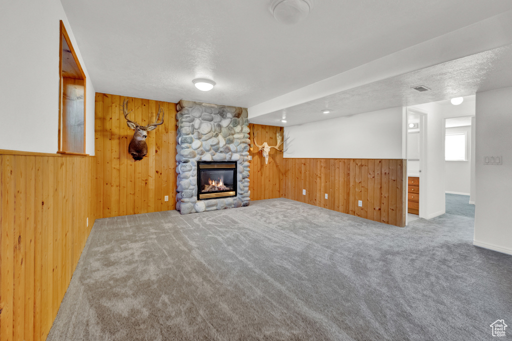 Unfurnished living room with wood walls, carpet, and a stone fireplace