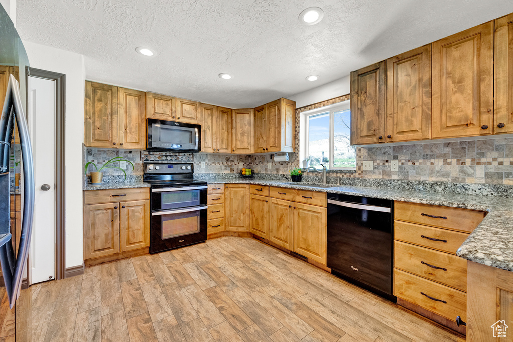 Kitchen featuring sink, backsplash, black appliances, light hardwood / wood-style flooring, and light stone countertops