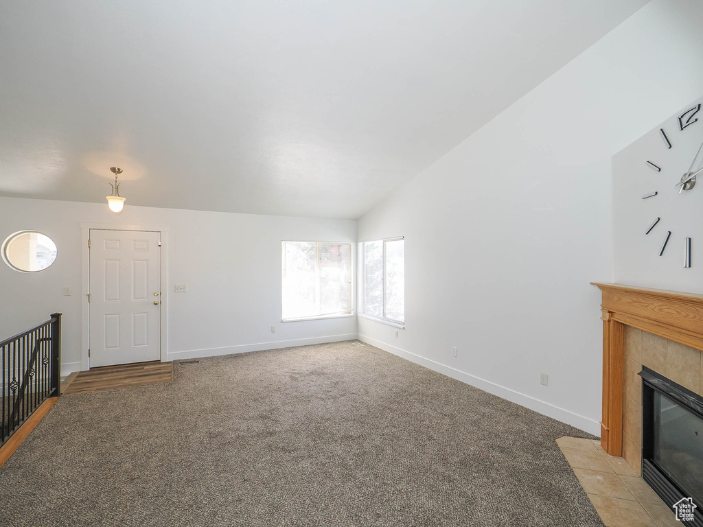 Unfurnished living room with light colored carpet, lofted ceiling, and a tile fireplace