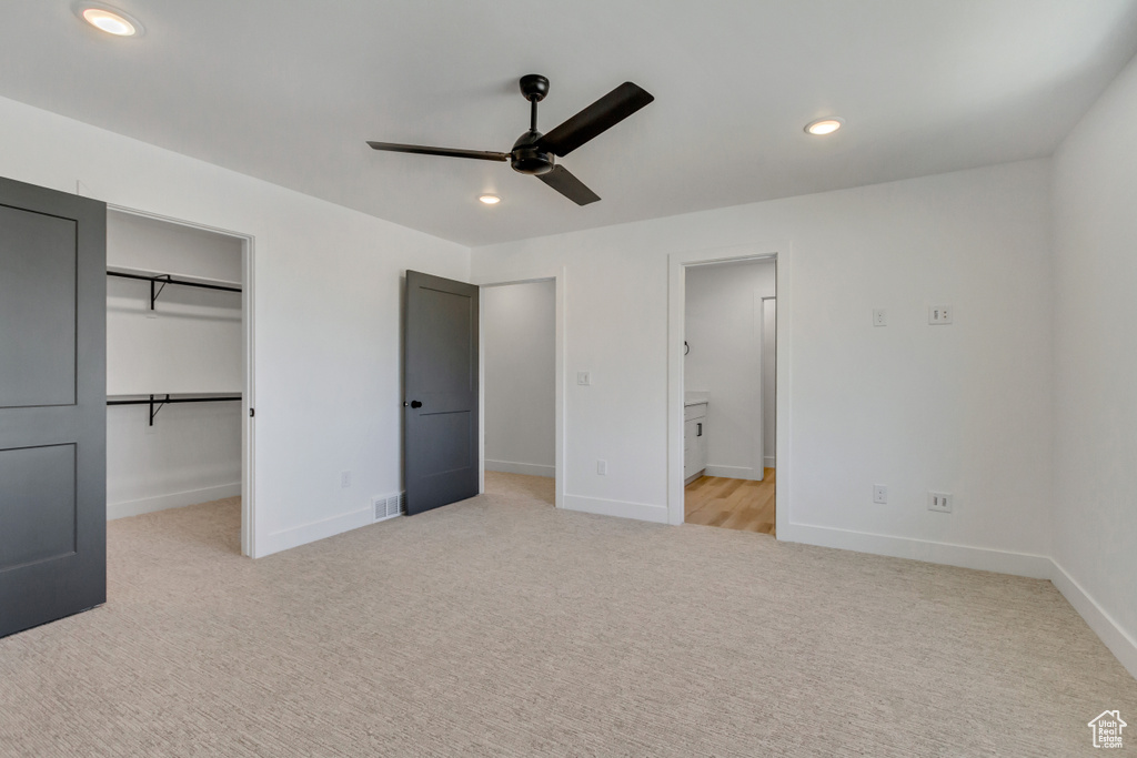 Unfurnished bedroom featuring light colored carpet, ceiling fan, a walk in closet, and a closet