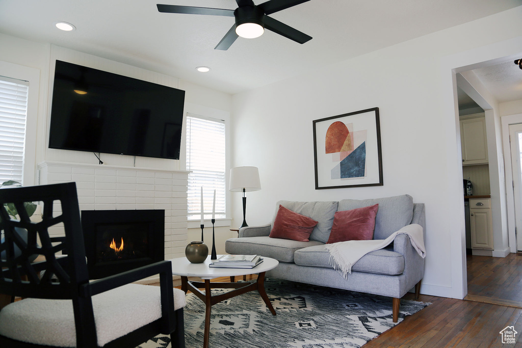 Living room with dark wood-type flooring, a brick fireplace, and ceiling fan