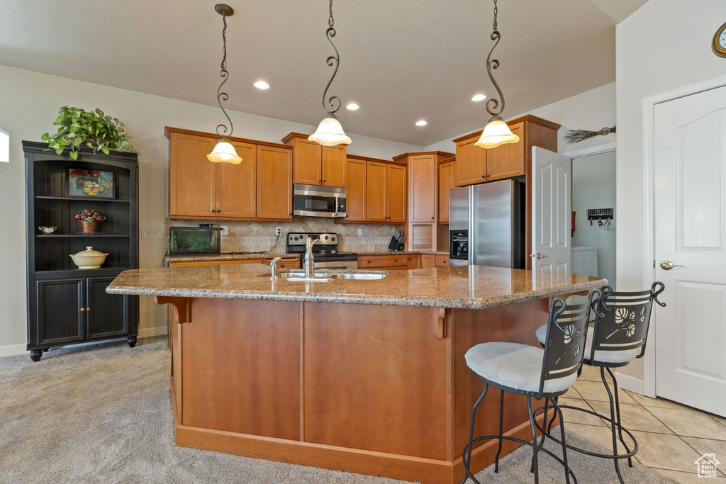 Kitchen with decorative light fixtures, appliances with stainless steel finishes, a kitchen island with sink, tasteful backsplash, and light stone counters