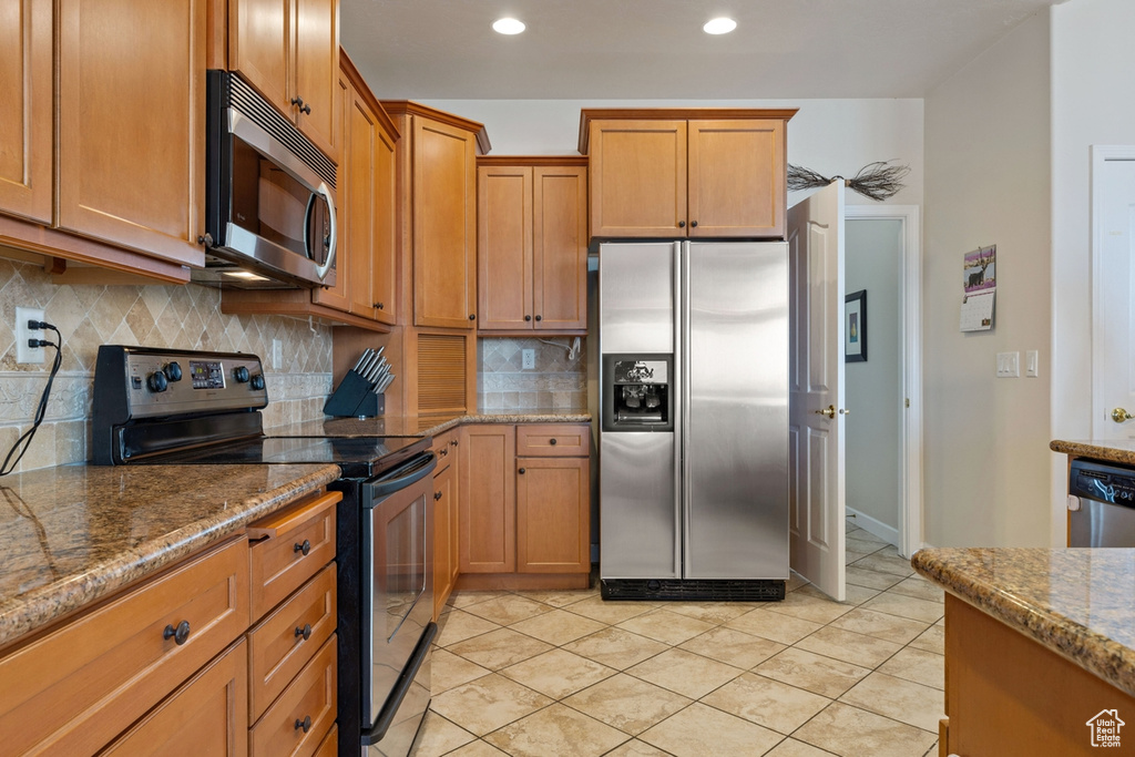 Kitchen with appliances with stainless steel finishes, tasteful backsplash, light tile floors, and stone counters