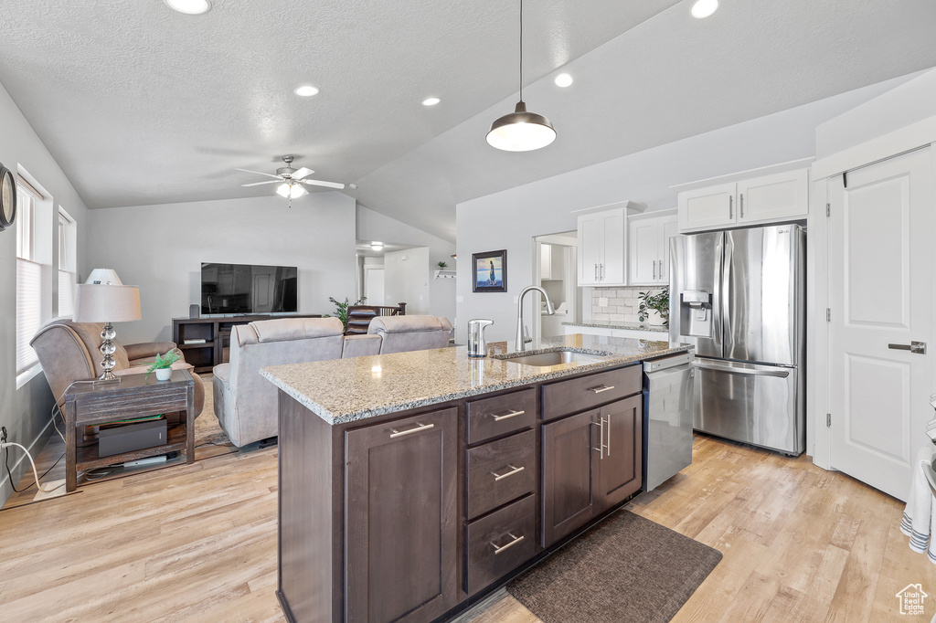 Kitchen with white cabinets, vaulted ceiling, light hardwood / wood-style flooring, and stainless steel appliances
