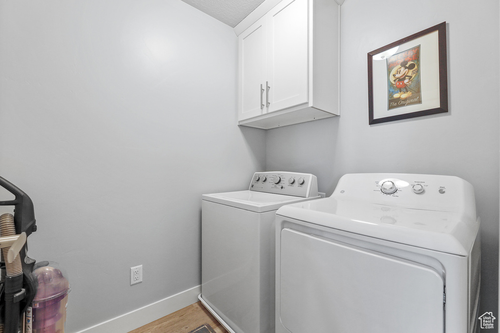 Laundry area with light hardwood / wood-style flooring, cabinets, and separate washer and dryer