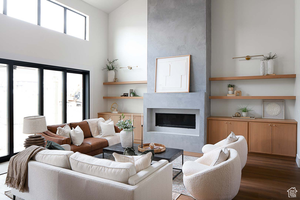 Living room featuring a large fireplace, dark hardwood / wood-style floors, built in features, and a towering ceiling