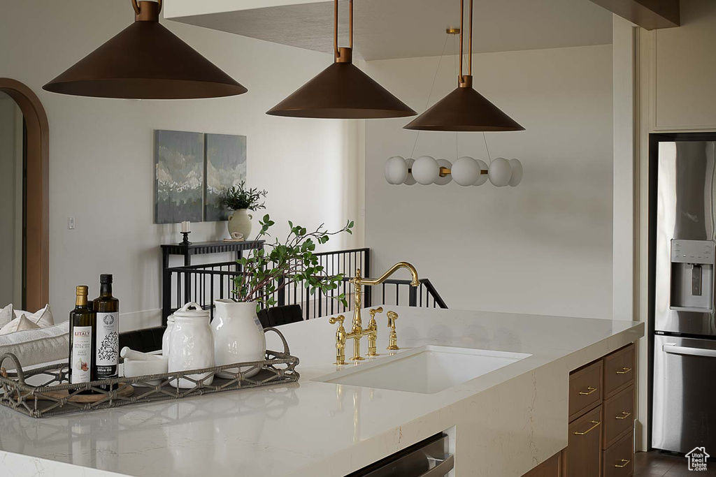 Kitchen with stainless steel fridge with ice dispenser, dark brown cabinets, hardwood / wood-style flooring, light stone countertops, and sink