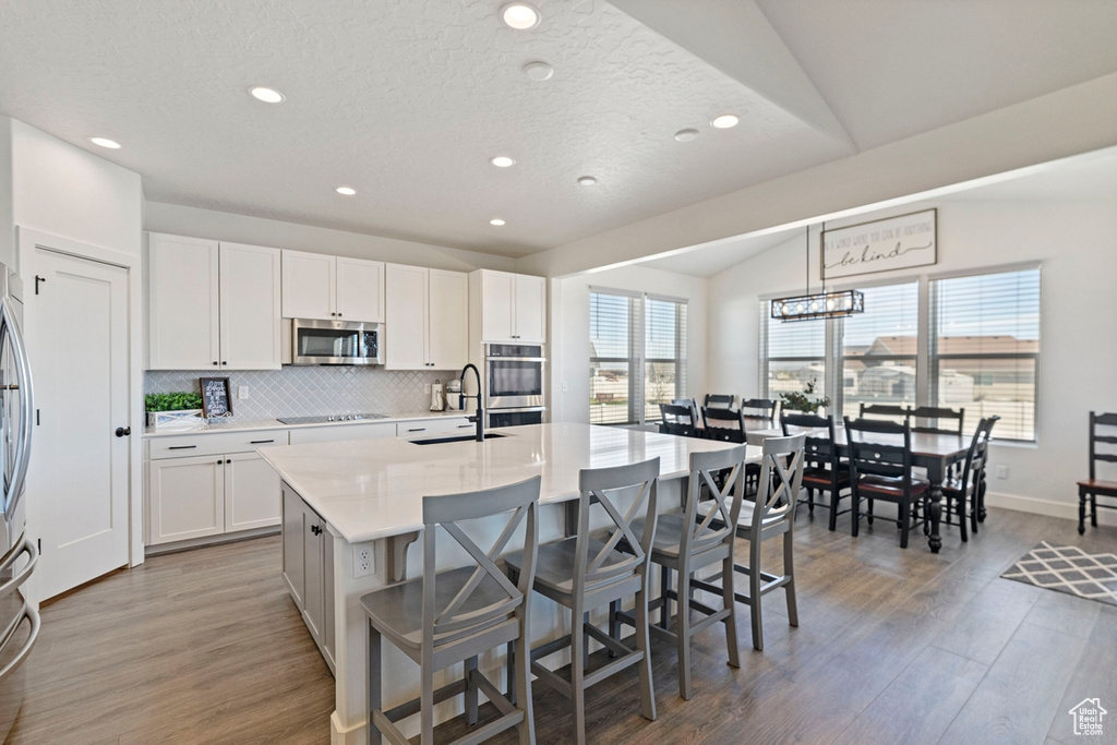 Kitchen featuring white cabinets, lofted ceiling, stainless steel appliances, and a kitchen island with sink
