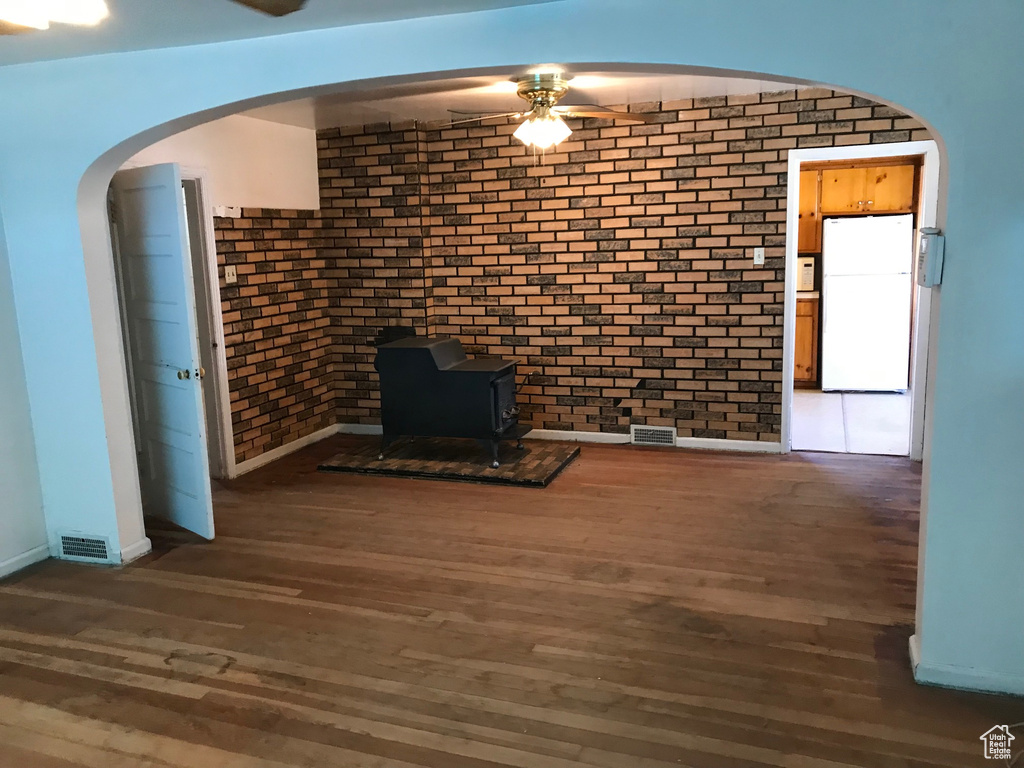 Unfurnished living room with ceiling fan, dark wood-type flooring, and brick wall