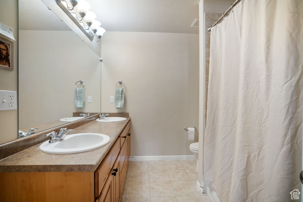 Bathroom featuring large vanity, tile floors, toilet, and dual sinks
