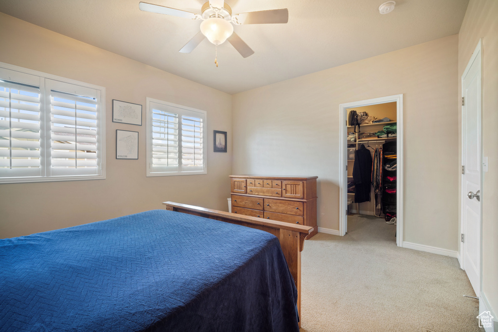 Bedroom featuring light colored carpet, a walk in closet, ceiling fan, and a closet