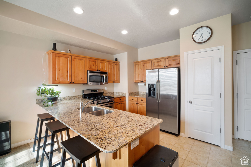 Kitchen with appliances with stainless steel finishes, light stone counters, a breakfast bar, sink, and light tile floors