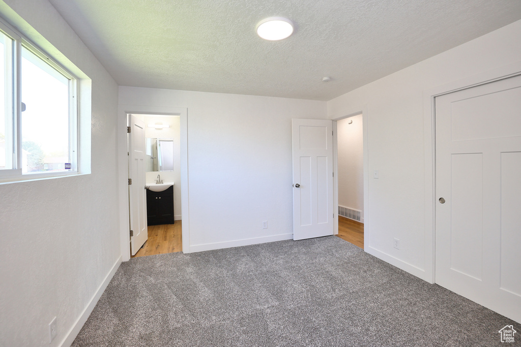 Unfurnished bedroom with light colored carpet, a textured ceiling, sink, and ensuite bathroom
