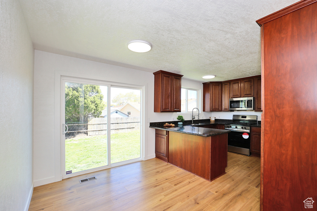 Kitchen with light hardwood / wood-style floors, appliances with stainless steel finishes, sink, and a textured ceiling