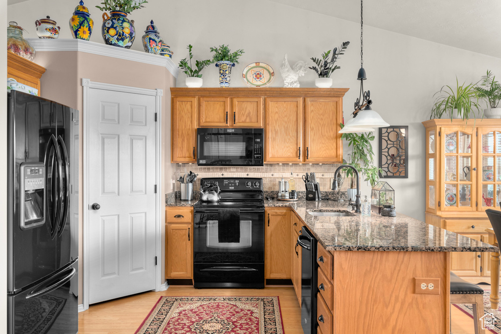 Kitchen featuring light hardwood / wood-style floors, backsplash, black appliances, vaulted ceiling, and dark stone countertops
