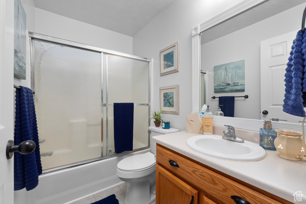 Full bathroom featuring vanity with extensive cabinet space, toilet, tile floors, and bath / shower combo with glass door