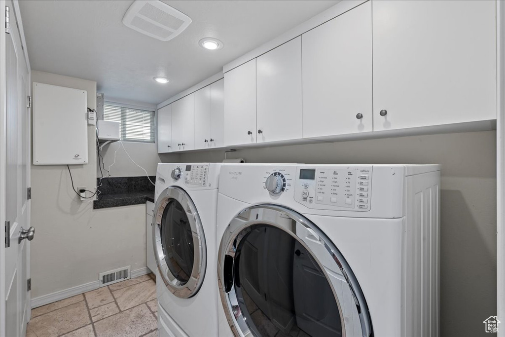 Laundry room featuring independent washer and dryer, cabinets, and light tile flooring
