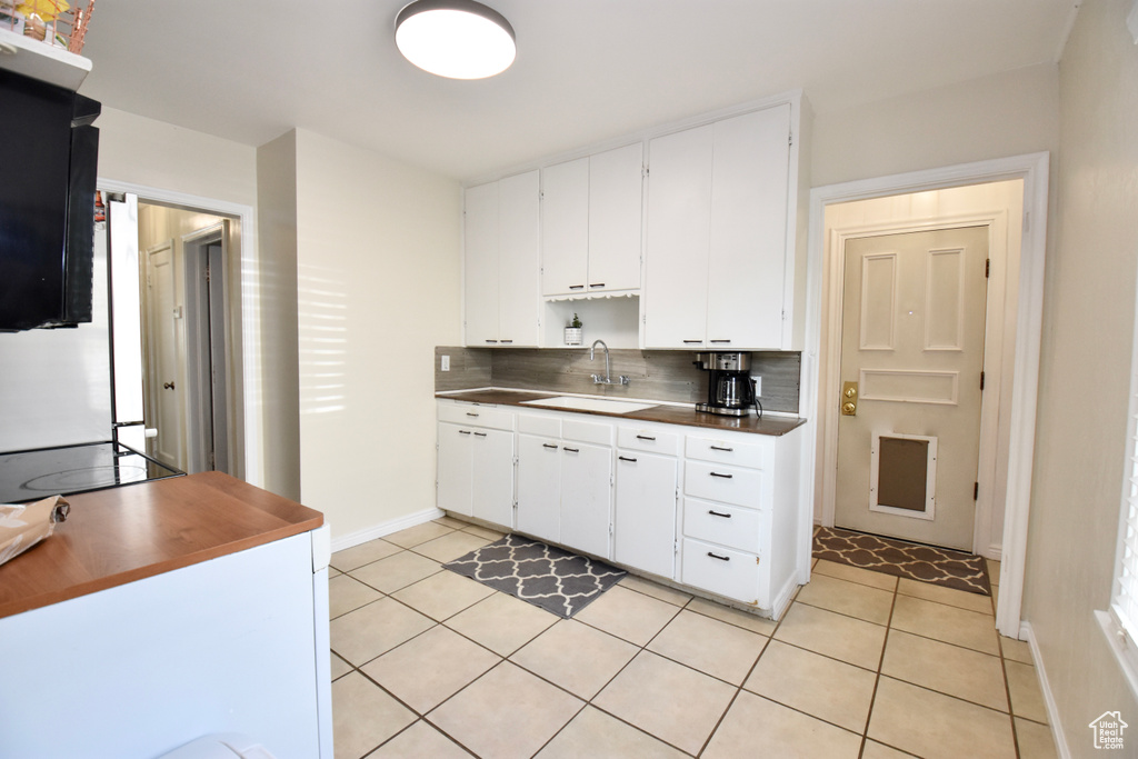 Kitchen with stove, white cabinetry, light tile floors, sink, and tasteful backsplash