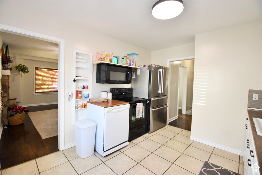 Kitchen with light tile floors, high quality fridge, white dishwasher, and range with electric stovetop