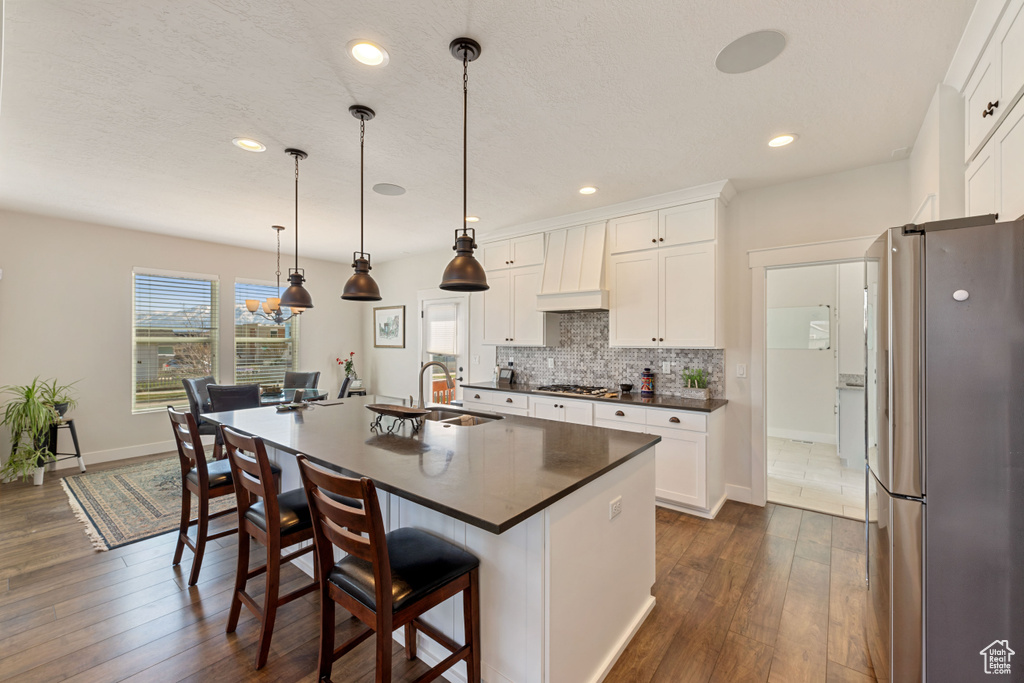 Kitchen featuring pendant lighting, white cabinetry, stainless steel appliances, a kitchen bar, and an island with sink