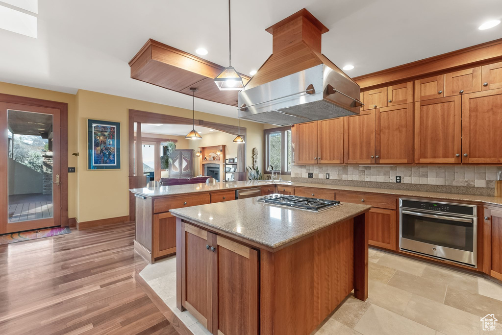 Kitchen featuring appliances with stainless steel finishes, a kitchen island, tasteful backsplash, light wood-type flooring, and pendant lighting