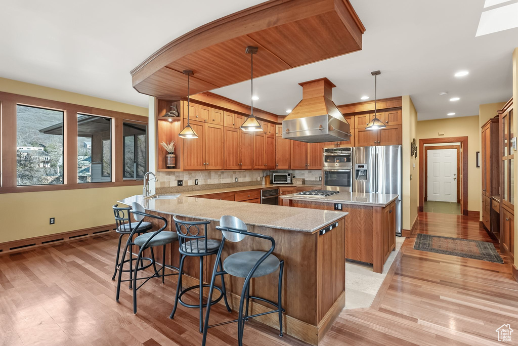 Kitchen featuring decorative light fixtures, backsplash, island range hood, sink, and light wood-type flooring