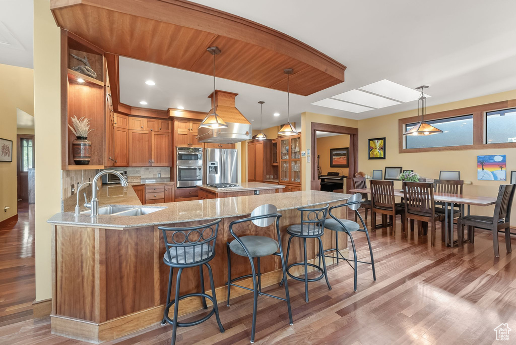 Kitchen featuring hanging light fixtures, light hardwood / wood-style flooring, backsplash, appliances with stainless steel finishes, and sink