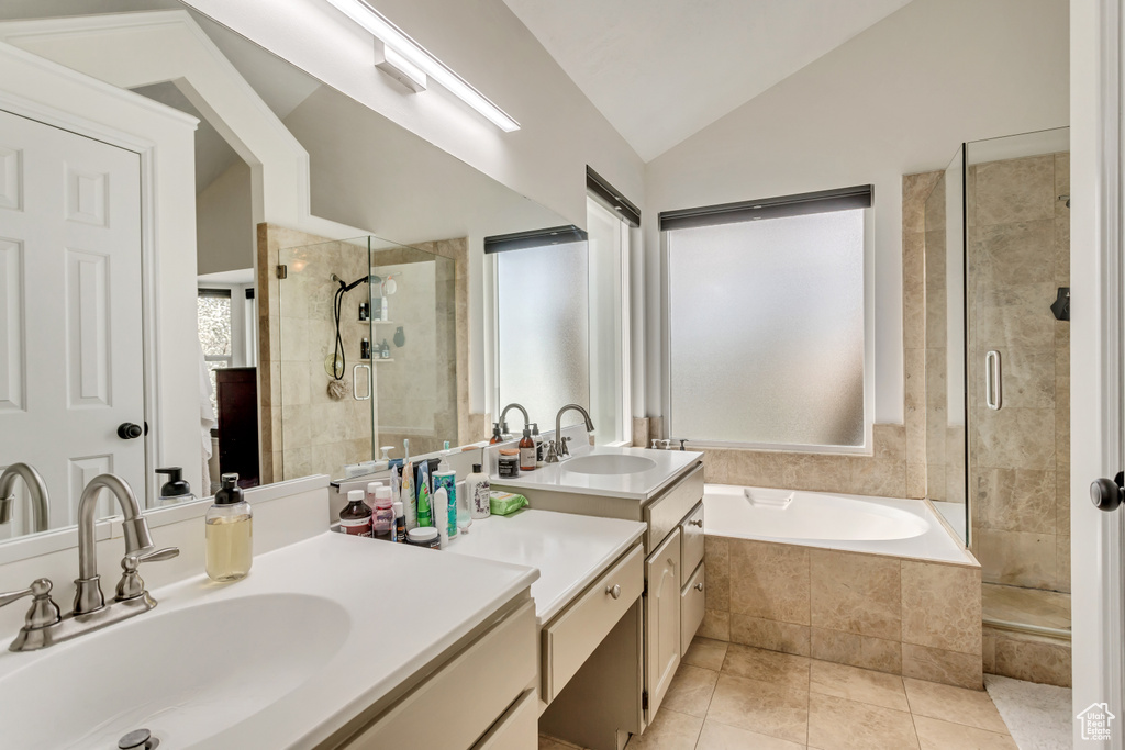 Bathroom with oversized vanity, lofted ceiling, shower with separate bathtub, tile floors, and dual sinks
