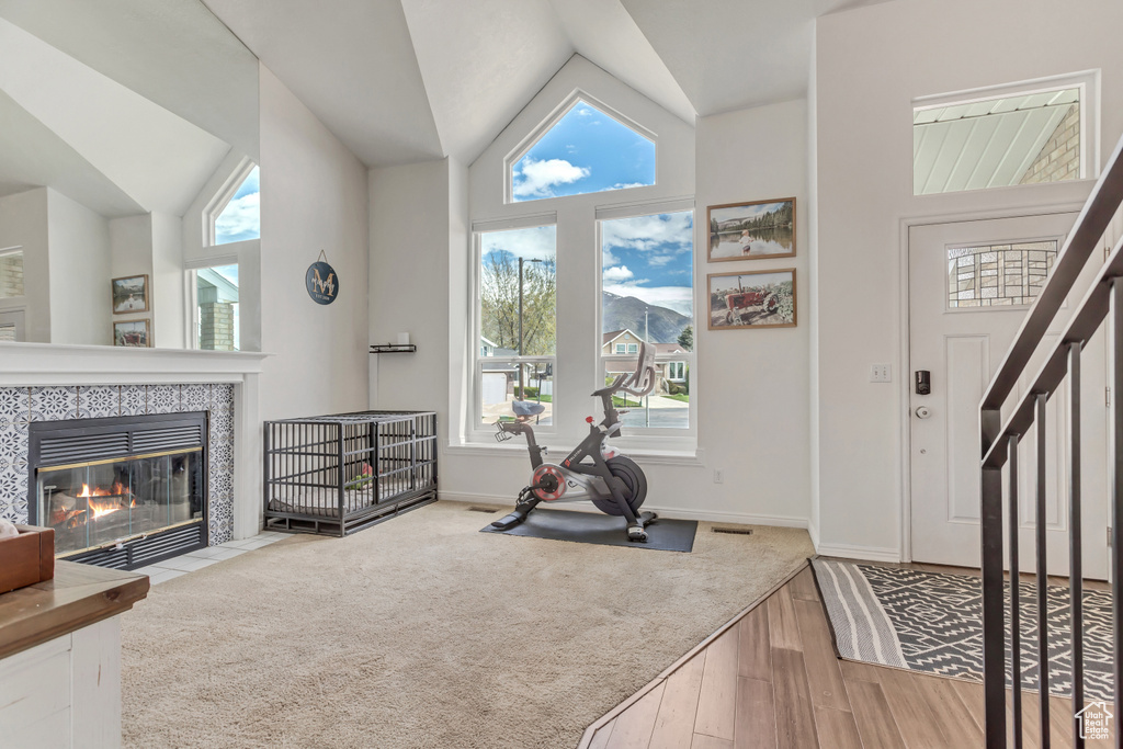 Exercise room with high vaulted ceiling, light hardwood / wood-style floors, and a tile fireplace