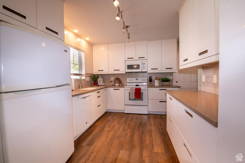 Kitchen with sink, white appliances, white cabinetry, dark hardwood / wood-style floors, and track lighting