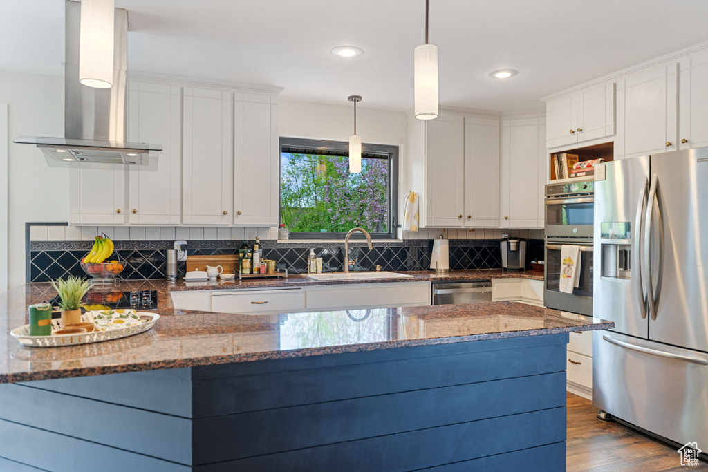 Kitchen with appliances with stainless steel finishes, island range hood, tasteful backsplash, dark stone counters, and sink