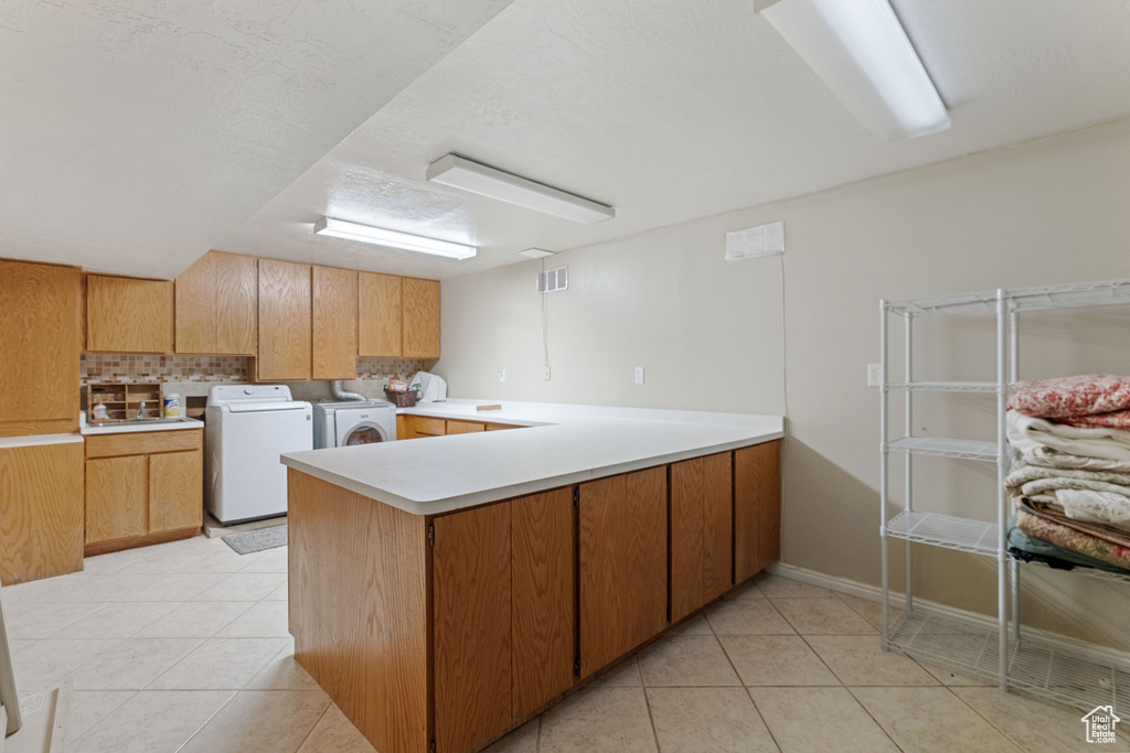 Kitchen featuring washer and dryer, light tile floors, kitchen peninsula, and tasteful backsplash