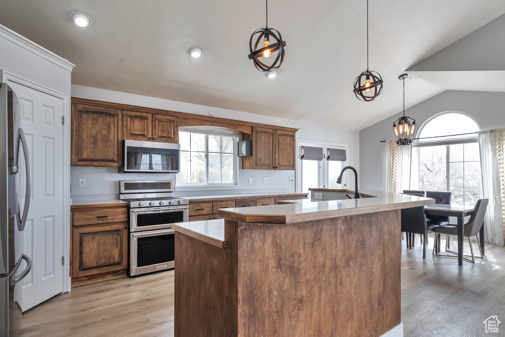 Kitchen featuring pendant lighting, a kitchen island with sink, stainless steel appliances, vaulted ceiling, and light hardwood / wood-style floors